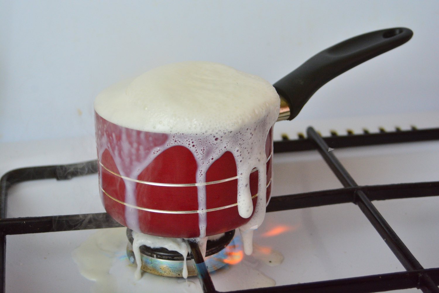 A small red pot overflowing with boiling milk